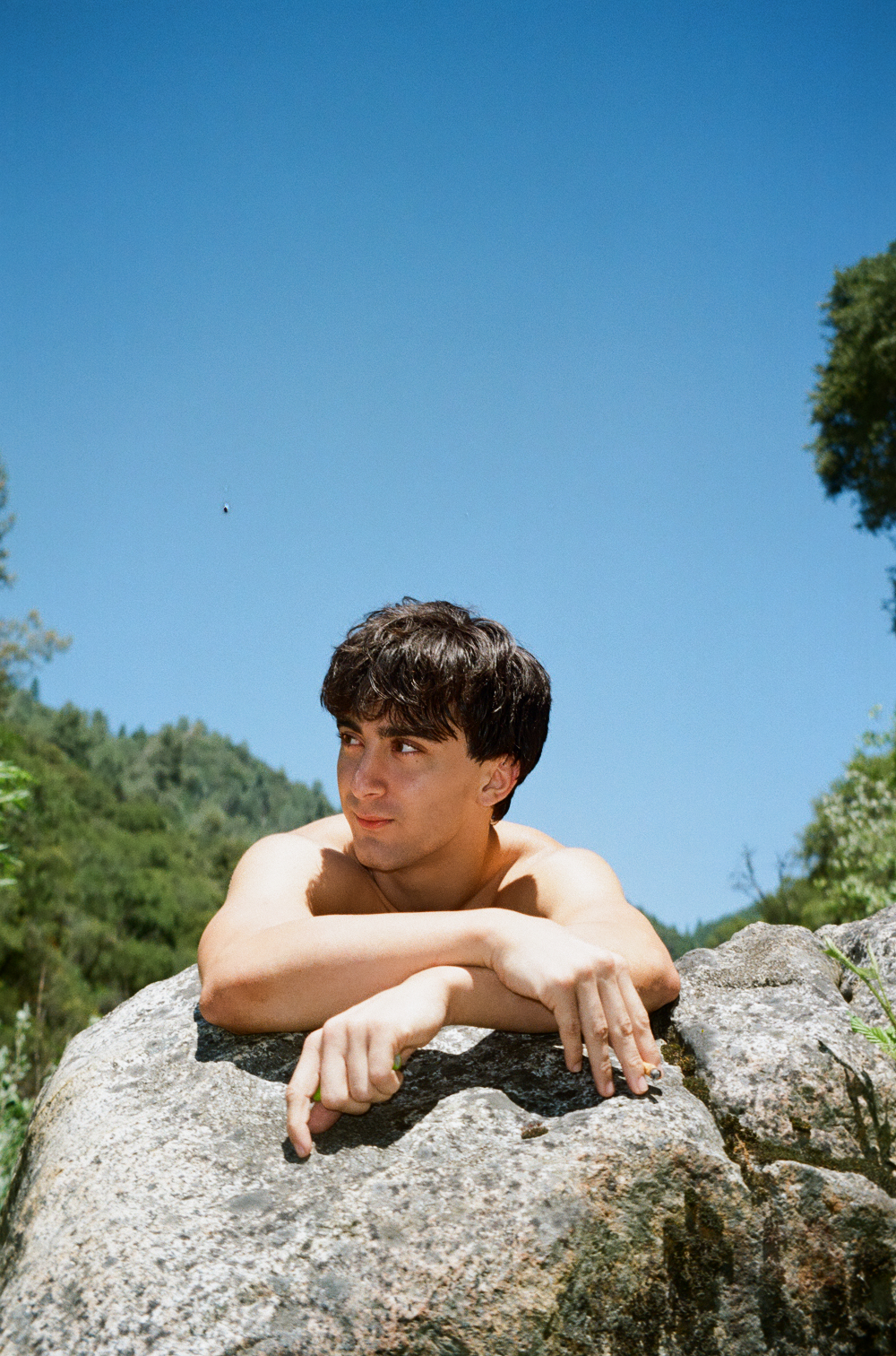 A young man resting on a rock against a blue sky