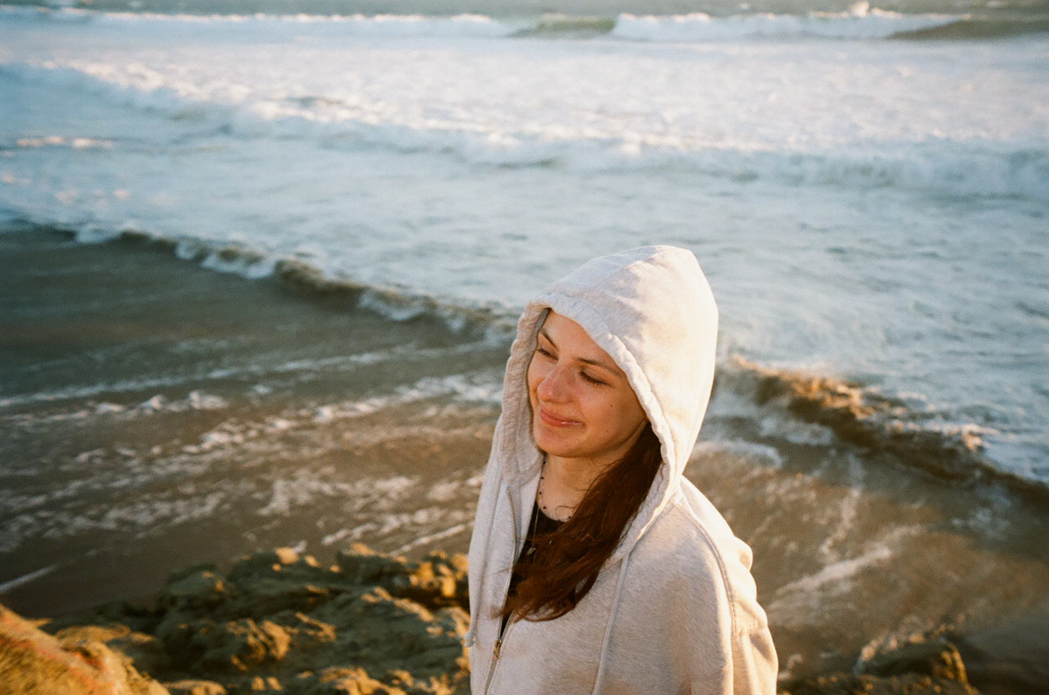 Woman in a hooded sweatshirt at the edge of the sea